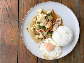Mix of fried vegetables, Cauliflower, Carrot, Sugar Pea with seafood with rice and fried egg in white plate on wooden background. Thai style food.