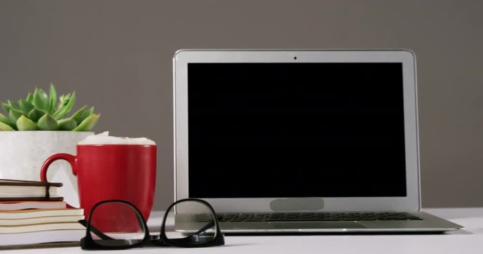 Laptop, spectacles, cup of coffee and stack of books