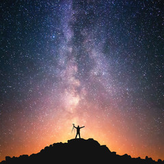 The Man and the Universe. A person is standing on the top of the hill next to the Milky Way galaxy with a tripod in his hands. - 165523392