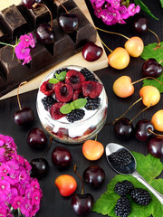 Oatmeal with yogurt and berries in a jar surrounded by berries and pink flowers. Layered breakfast