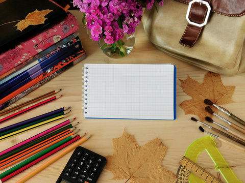 School supplies on a wooden table. Notebook with a blank page in the middle