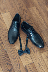 Black leather shoes and bow tie stand on wooden floor