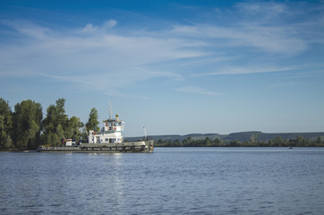 A Russian ship sails along the river under a blue sky with white clouds.