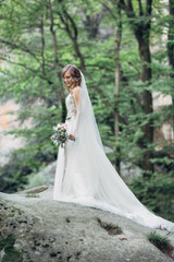 Bride stands alone in the summer forest