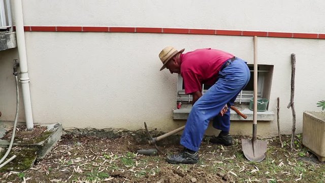 Homme travaille dans son jardin avec une pioche.