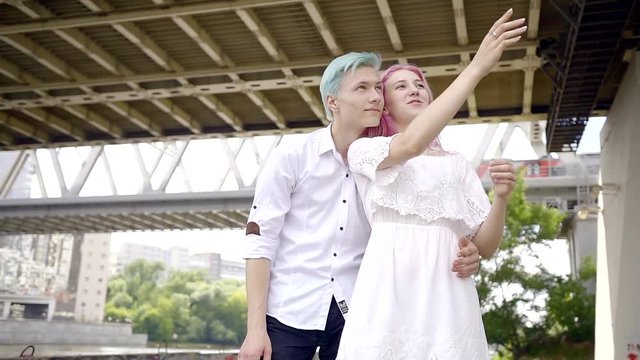 young boys with bright hair color, blue and pink are considering ahead and show a gesture of the arm that the watch. walk around the modern city.