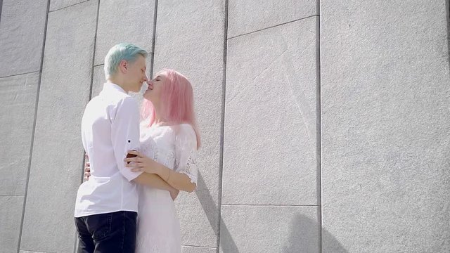 couple of hipsters hugging a stone high wall. their hair bright colors pink and blue