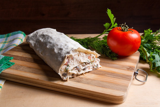 Pita bread or lavash wrapped with cottage cheese or curd, chicken, tomatoes and herbs - dill, onion, parsley on cutting board..