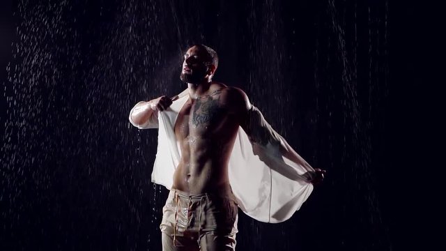 muscular male bodybuilder takes wet body white shirt standing in the night under a big rain. large inflated Breasts