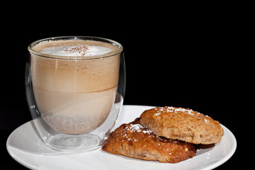 Coffee break. Cappuccino coffee and home-made biscuits on a white plate against black background.