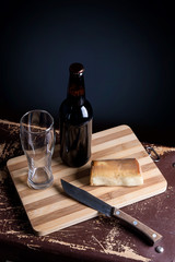 Glass and Bottle of dark beer with smoked cheese on cutting board.