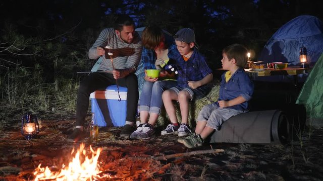 campground, family communicates and putting marshmallows on skewer near fire in forest, husband and wife with kids puts zephyr to skewer near campfire, parent with children enjoying in camping,