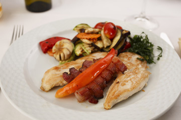 Chicken with bacon and grilled vegetables arranged on a plate, Traditional dish in elegant setting, Selective focus with soft light