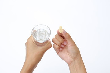 Hand holding yellow pill with water in glass isolated on white background.