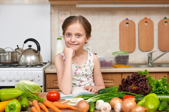 child girl with fruits and vegetables in home kitchen interior, read cooking book, healthy food concept