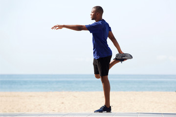 Fit young african man doing warm up exercise on beach