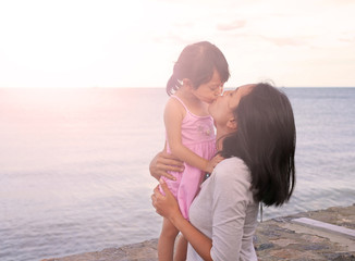 mother and kid girl kissing with natural emotion smiling on sea background in the evening.