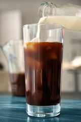 Pouring milk into glass with cold brew coffee on wooden table