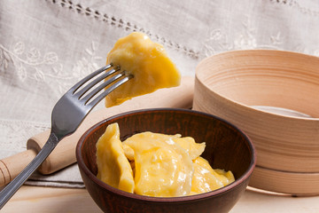 Close up view of boiled varenyky or dumpling with cottage cheese or curd on metal fork. Fresh boiled homemade ukrainian dumplings in clay bowl on wooden background..