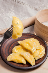 Close up view of boiled varenyky or dumpling with cottage cheese or curd on metal fork. Fresh boiled homemade ukrainian dumplings on clay plate on wooden background..