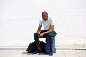 African man sitting on suitcase and looking at mobile phone