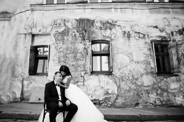 Naklejka na ściany i meble Handsome groom sitting on the chair with a beautiful bride standing beside. Awesome wedding.