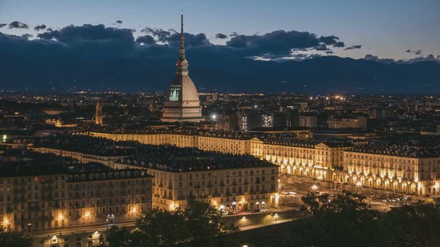 Torino (Turin, Italy) skyline with the Mole Antonelliana towering over the buildings. Timelapse fading from sunset to dusk, turning on city lights. Moving clouds over the Alps in the background.