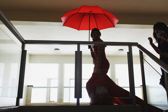Asian bride walks under red umbrella in the hall - Powered by Adobe