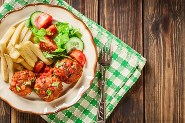 Roasted meatballs in tomato sauce with french fries and salad