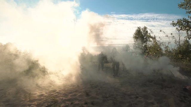 Silhouettes of soldiers walking on battlefield and aiming with guns through the smoke