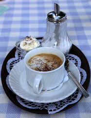 Cappuccino mit Sahne auf blau-weiß gemusterter Tischdecke, altmodisch