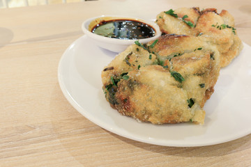 Fried Chinese pancake with black sweet chili sauce on white dish and wood table