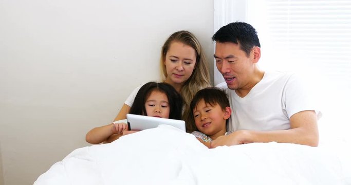 Happy family relaxing on bed and using digital tablet