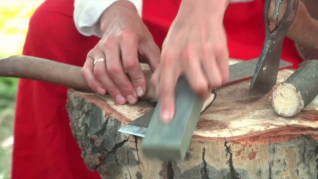 The man is engaged in Old Russian work. The man sharpens the axe for work.