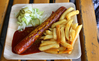 Currywurst mit Pommes und Salat auf Teller mit Ketchup 