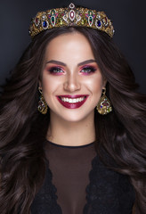 Beautiful brunette girl with a golden crown, earrings and professional evening color make-up and perfect smile. Beauty face. Miss world
