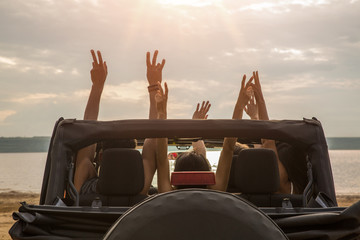 Friends sitting in a car with hands raised - obrazy, fototapety, plakaty