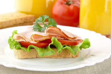 Toast,lettuce,tomato,cold cuts on plate with orange juice on lin