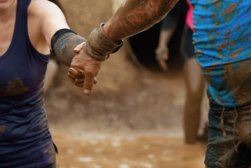 Mud race runners.The man helps the woman to overcome the obstacle