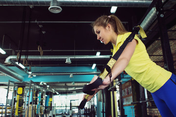 Young woman athlete trains using TRX, workout. On background of interior