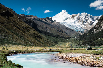 turquoise mountain river in the Cordillera Blanca in the Andes in Peru in a beautiful mountain valley with high snowy peaks and forest in the background