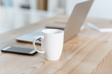 selective focus of coffee cup standing on table with digital devices in office