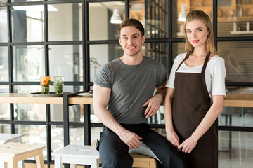 portrait of young waiter and waitress looking at camera in cafe