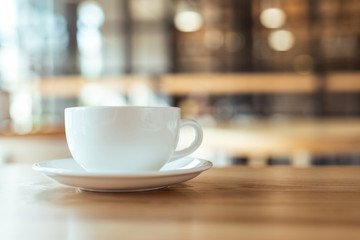 close up view of cup of coffee on saucer on wooden table in coffee shop