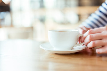 cropped shot of female hands holding cup of coffee on saucer