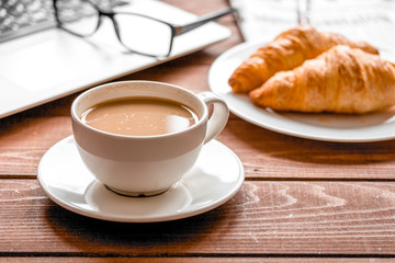 Business lunch with croissant and laptop on wooden desk