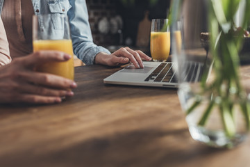 Cropped image of person sitting at kitchen table and using laptop