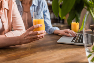 two women using laptop at table in kitchen, drinking juice - Powered by Adobe