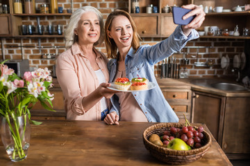 two women, senior and young taking selfie in kitchen