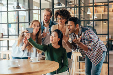 Young happy multiethnic friends taking selfie in cafe